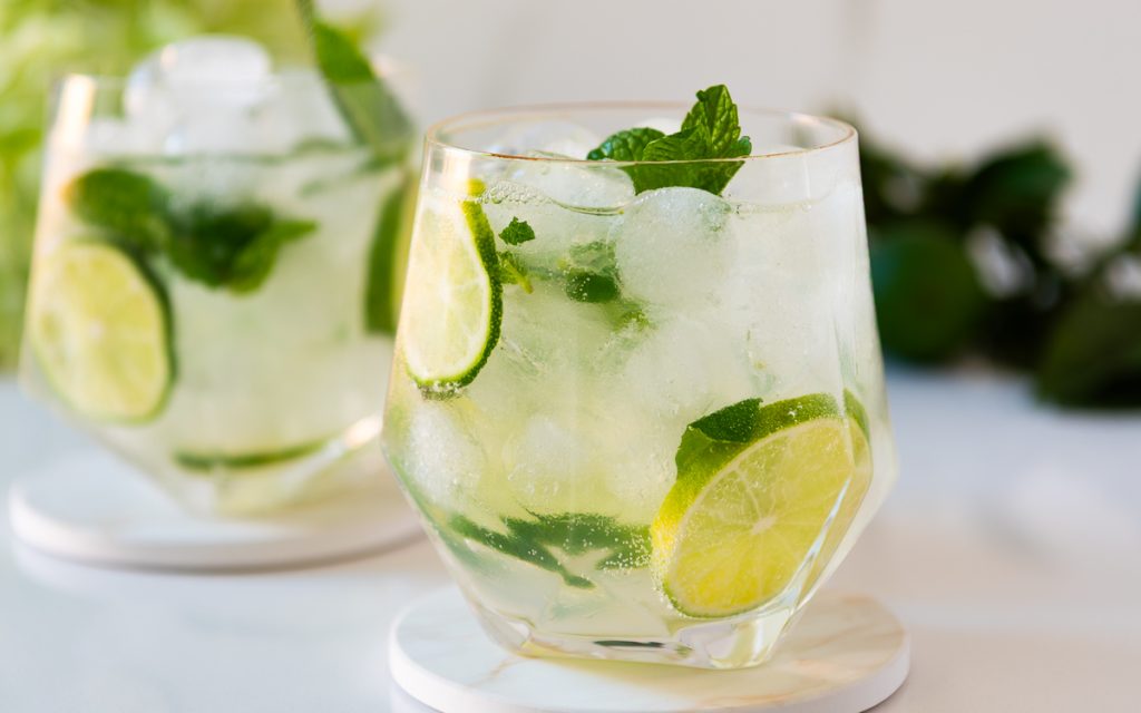 Two mojito mocktails with lime wedges and mint on a marble counter