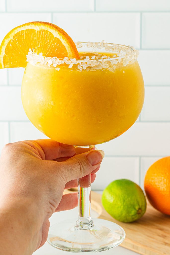 Hand holding salt rimmed glass of virgin mango margarita