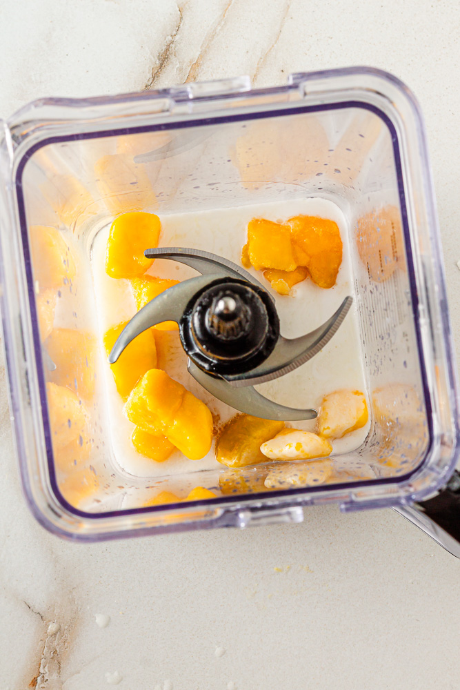 Blender with frozen mango, pineapple juice, coconut water, and coconut milk for tropical mocktail"