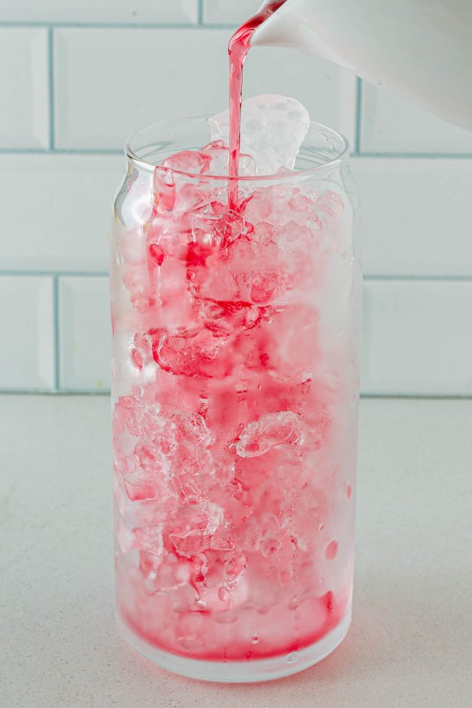 Filling a glass with ice to make a holiday cranberry mocktail