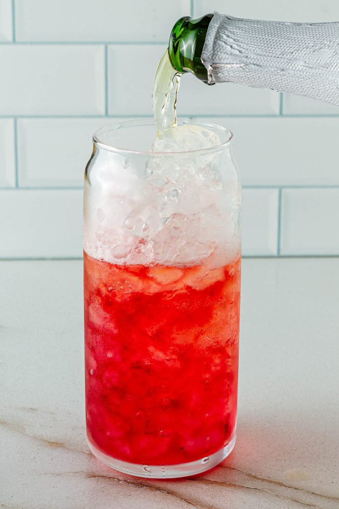 Topping off glass of cranberry juice with non-alcoholic champagne