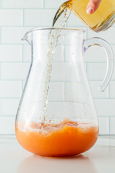 Adding gingerale to non-alcoholic punch recipe in large glass pitcher