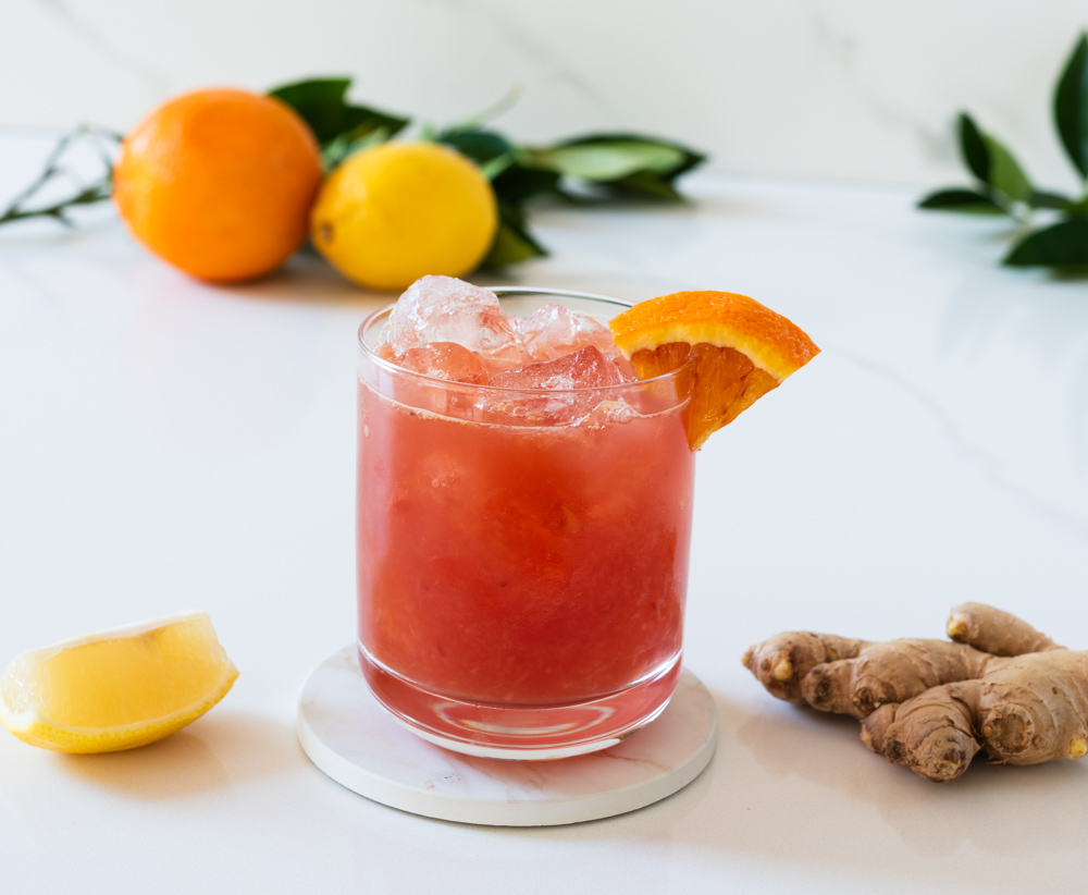 non-alcoholic blood orange mule mocktail surrounded by lemons and ginger