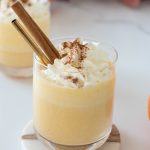 Glass of creamy pumpkin nog mocktail topped with whipped cream and cinnamon sticks – festive egg-free, alcohol-free holiday drink.