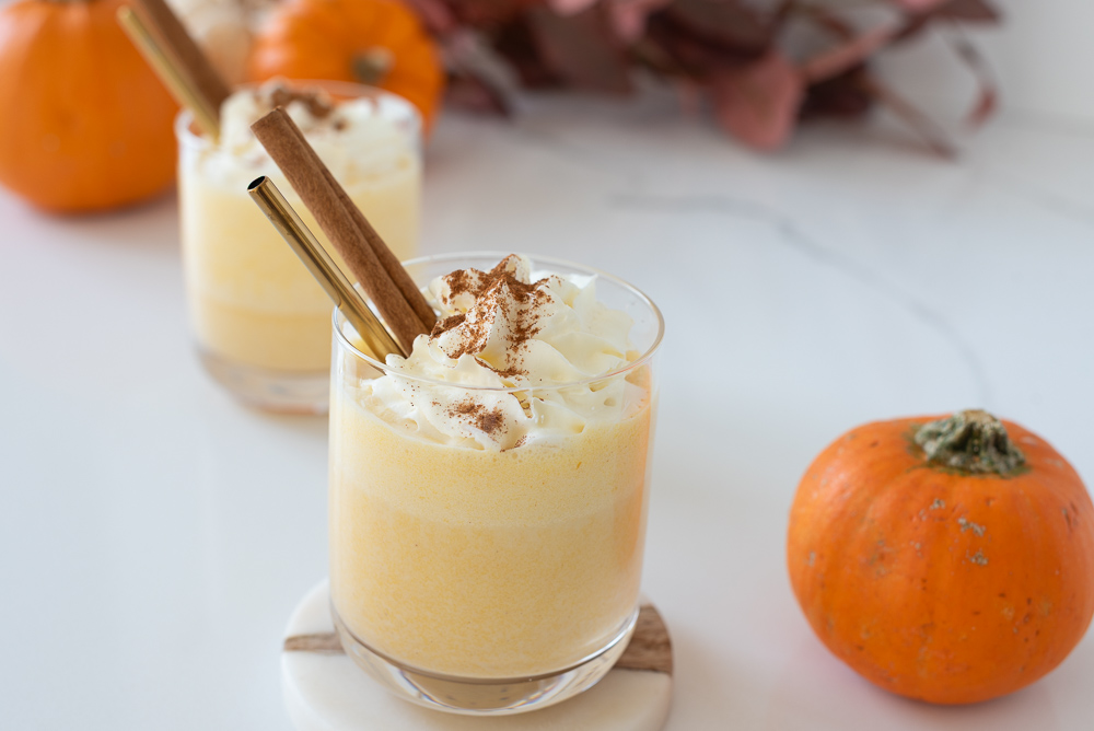 two glasses of creamy pumpkin nog mocktail topped with whipped cream and cinnamon sticks – festive alcohol-free holiday drink