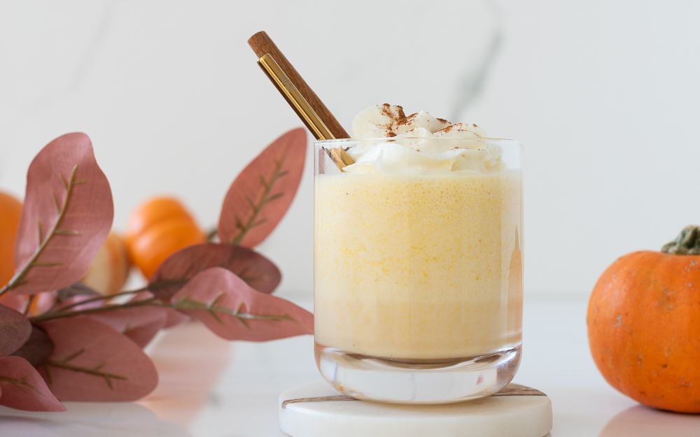 Glass of creamy pumpkin nog mocktail topped with whipped cream and cinnamon sticks – festive egg-free, alcohol-free holiday drink.