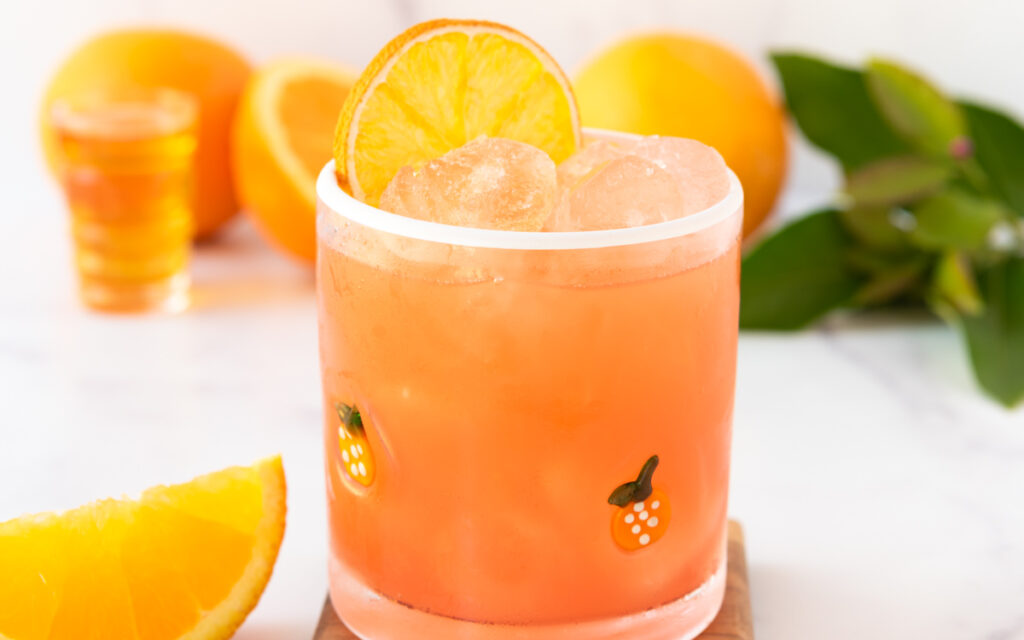 coral hued virgin margarita mocktail with a dried orange