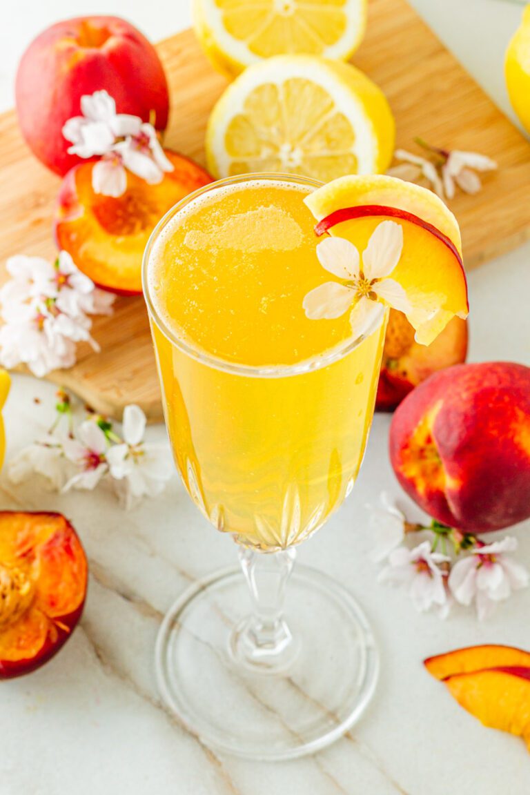 glass of peach bellini mocktail surrounded by peaches and white blossums