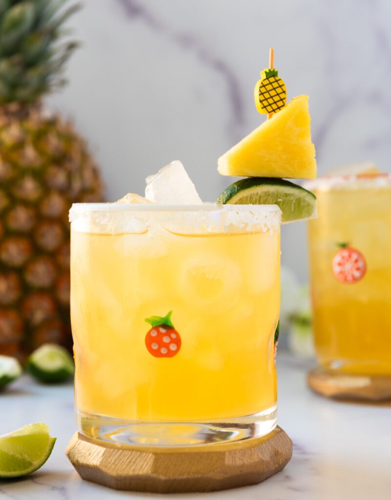 glass of non alcoholic pineapple margarita with chunks of fresh pineapple