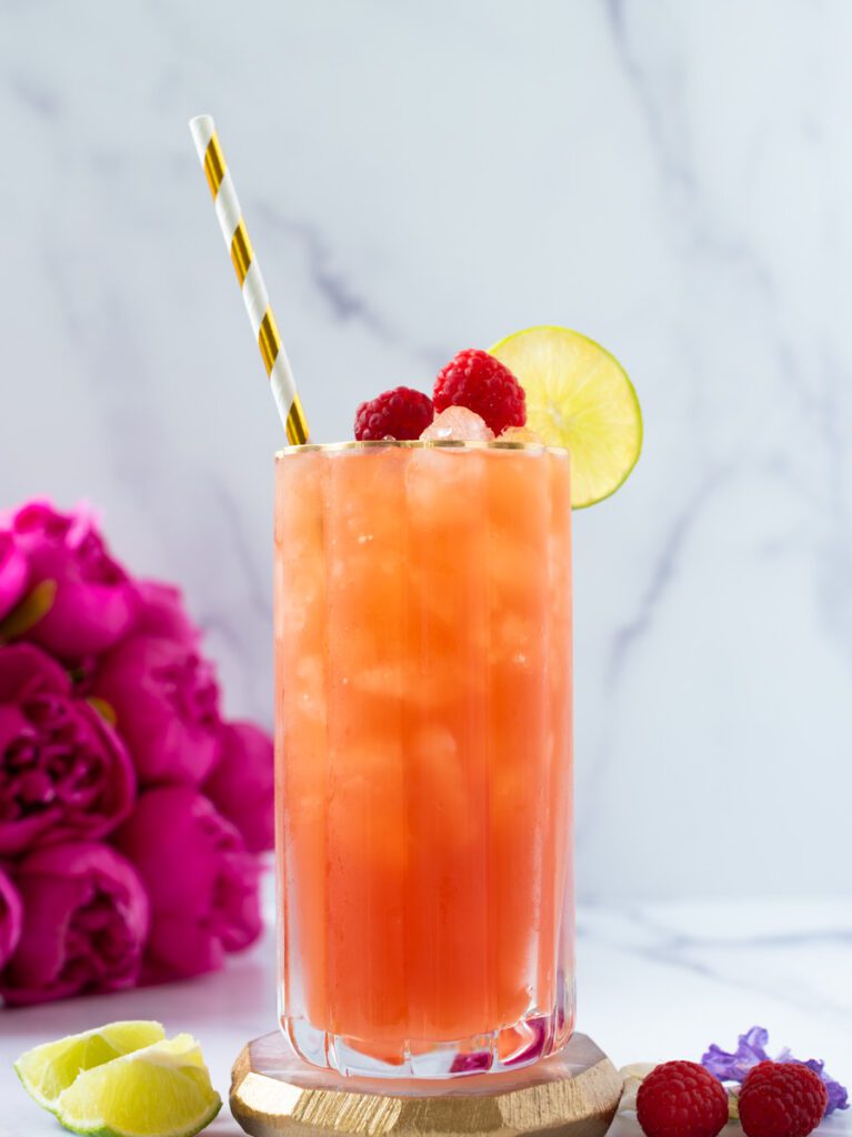 glass of raspberry mocktail with a gold and white straw and fresh berries