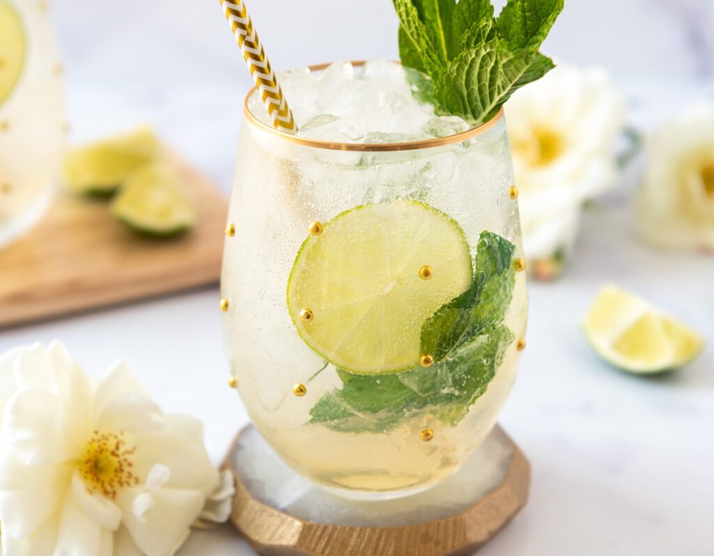 large glass of icy Hugo Spritz Mocktail with lime wheels and mint