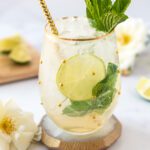 large glass of icy Hugo Spritz Mocktail with lime wheels and mint