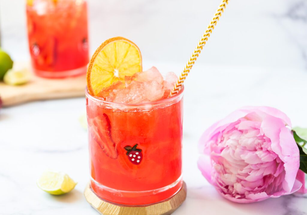 glass of pink virgin strawberry margarita mocktail with fresh citrus and a pink flower