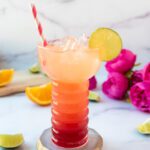 glass of strawberry pineapple spritz with pink flowers and pink and white straw